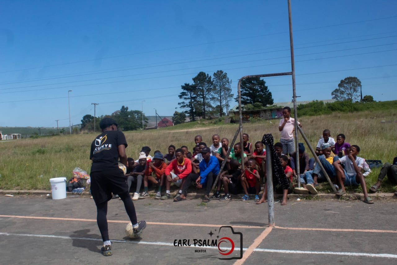 A coach demonstrating footwork to a group of young players seated on an outdoor court