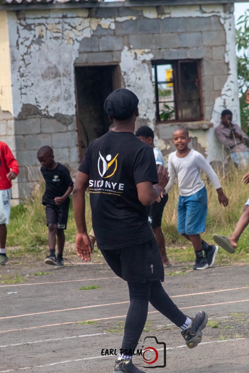 A coach in a Sikunye shirt moving across the court during a training session