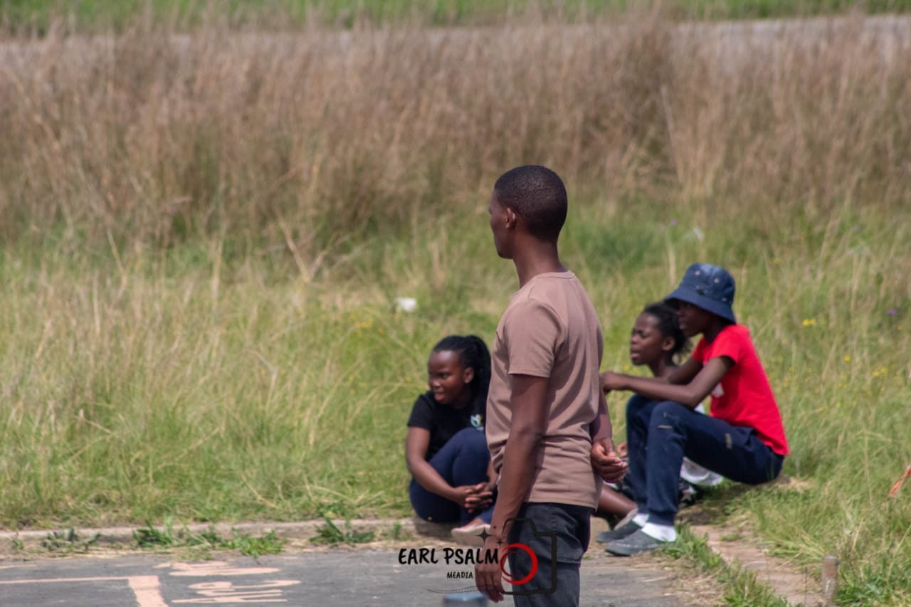 A boy standing at the edge of a court while two others rest on the grass behind him