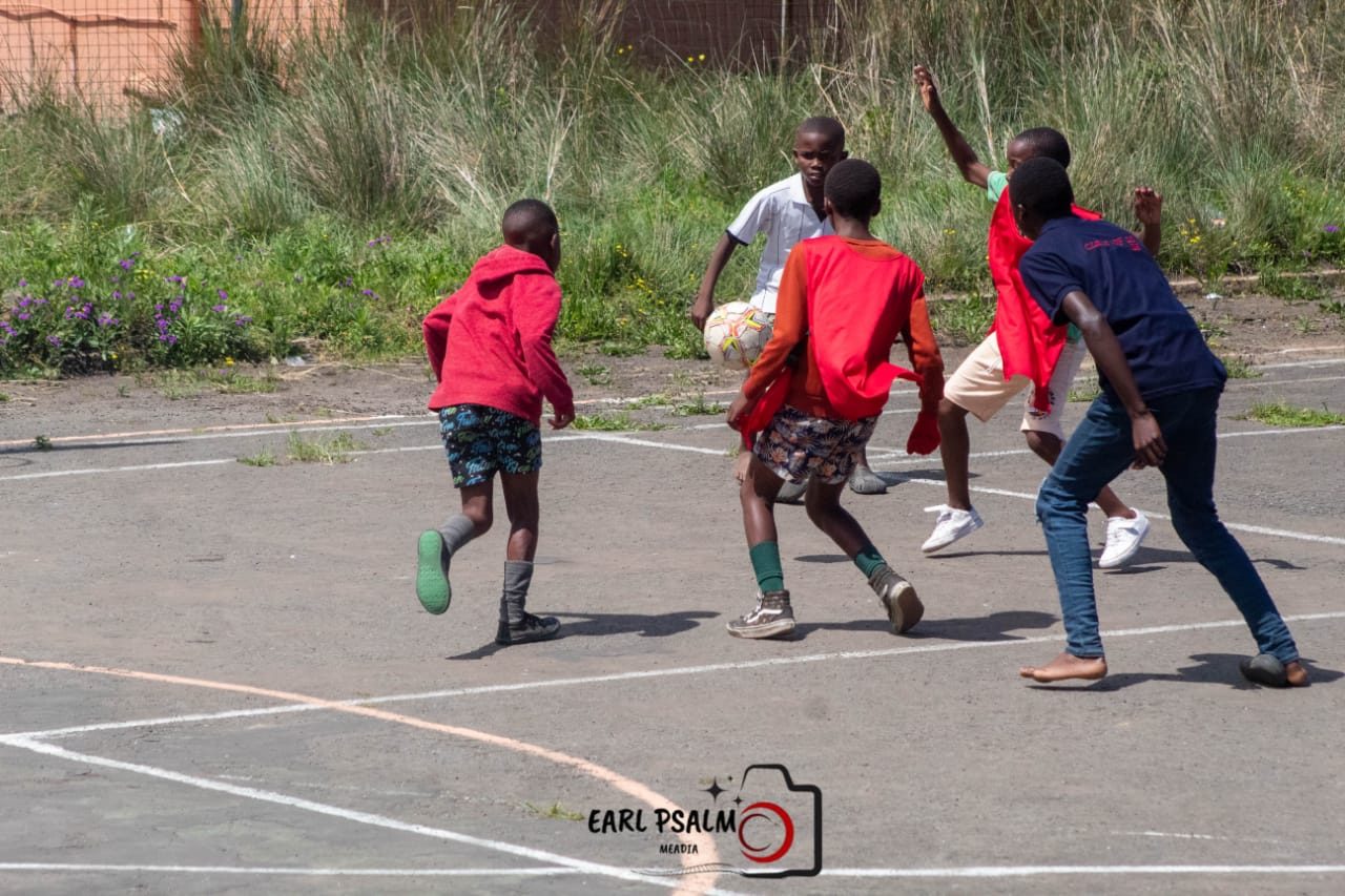 Young players contesting the ball during a soccer match on an asphalt court in Dimbaza