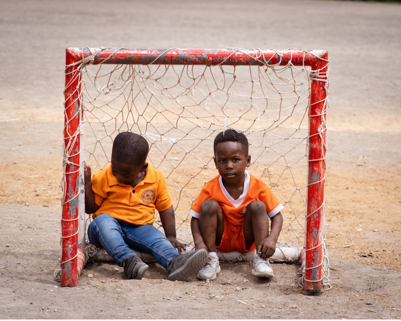 Two young boys sitting inside a small soccer goal