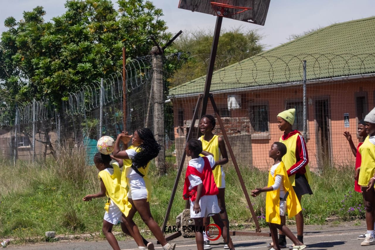 Girls playing netball under a wooden backboard on a neighbourhood court