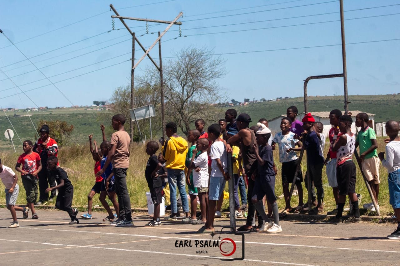 Children and teenagers lining the sideline of an outdoor court, watching the game