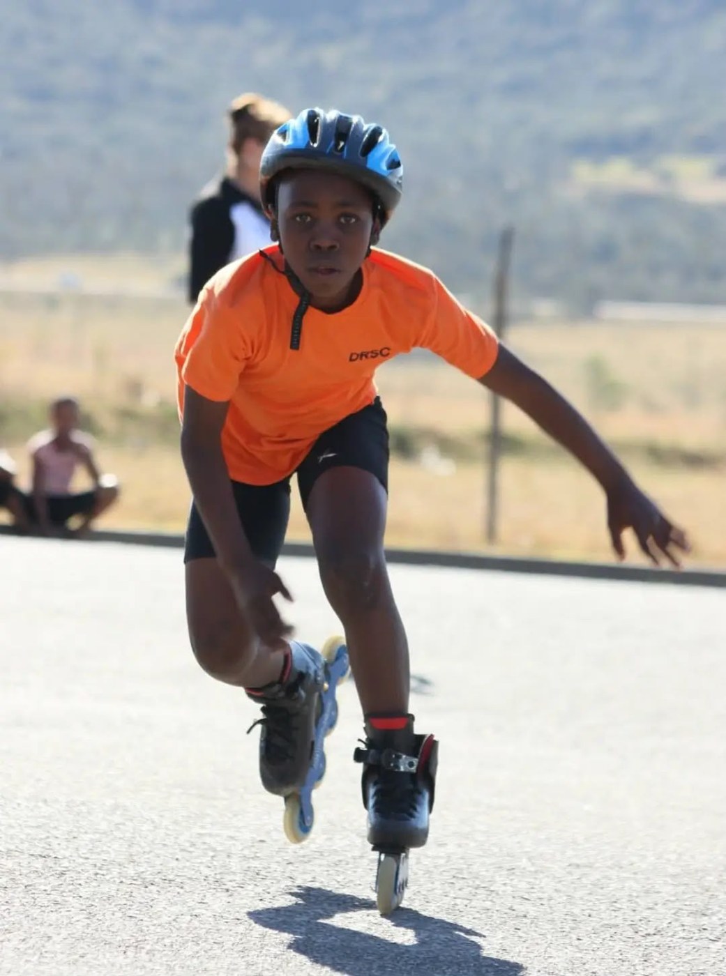 A young skater in an orange shirt and blue helmet skating on the road