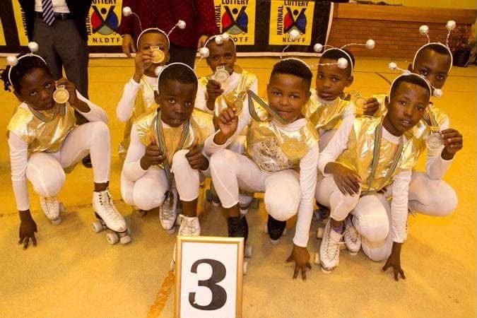 Young skaters in matching white and gold outfits displaying medals beside a third-place sign