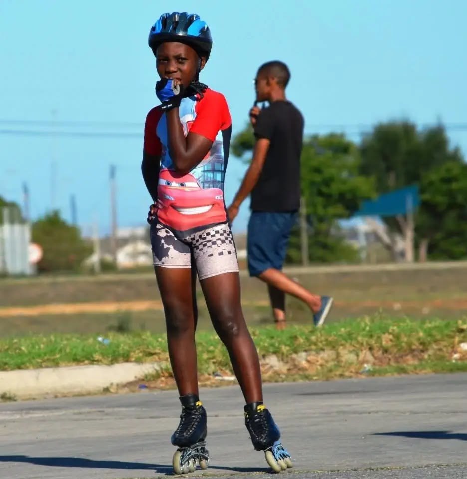 A young skater in a red shirt and helmet standing on inline skates