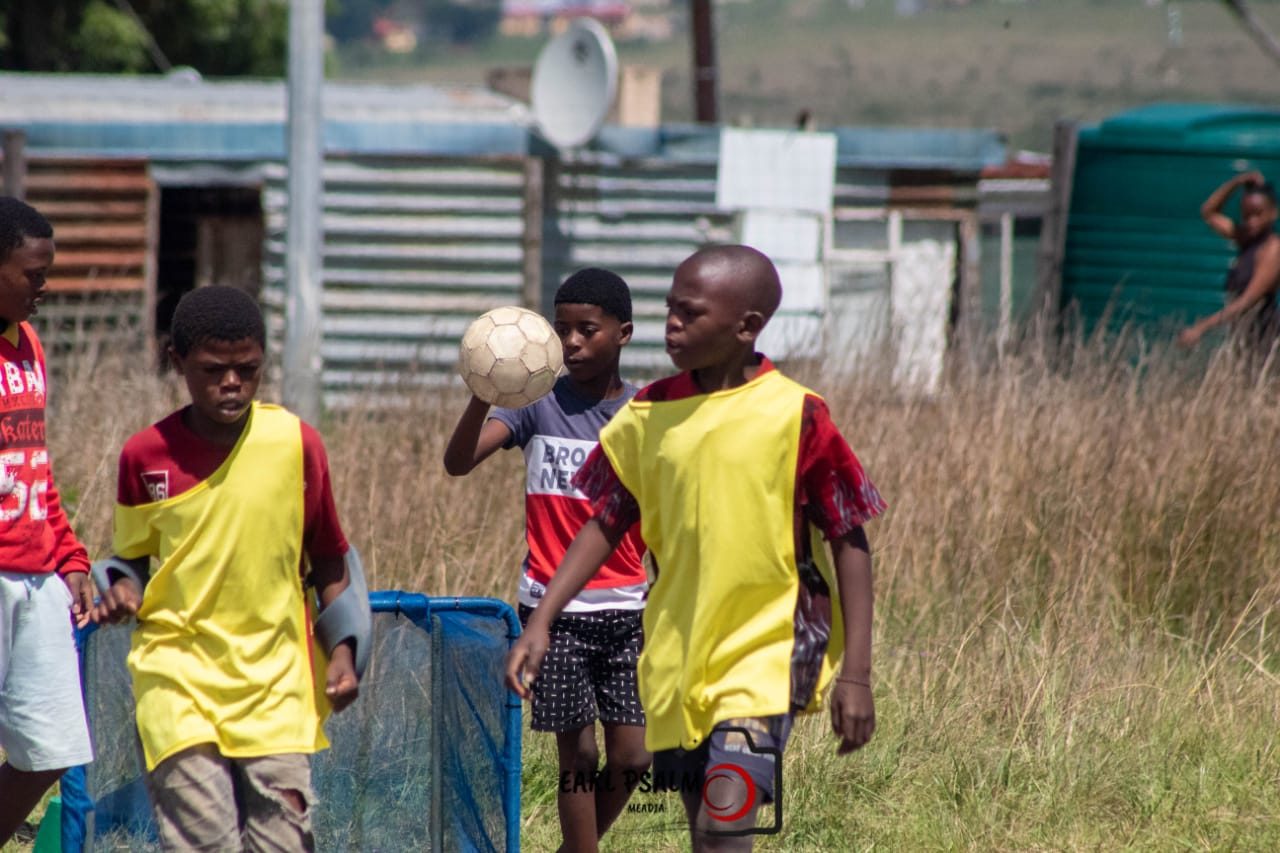 Children playing near a small blue training goal on a grass field